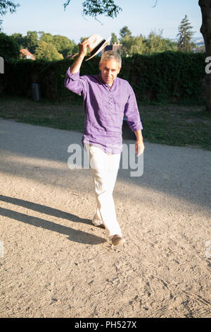 Happy man in straw hat walking near hedgerow Stock Photo