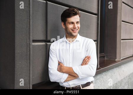 Smiling young male manager formal dressed leaning on a wall outdoors Stock Photo
