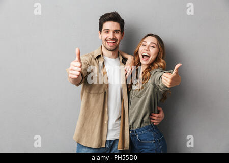 Happy young couple showing thumbs up and looking at camera isolated over gray background Stock Photo