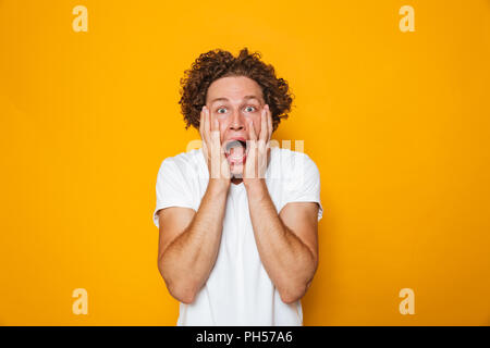 Portrait of a shocked curly haired man screaming isolated over yellow background Stock Photo