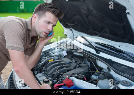young stressed man having trouble with his broken car looking in frustration and calling to special services for help Stock Photo