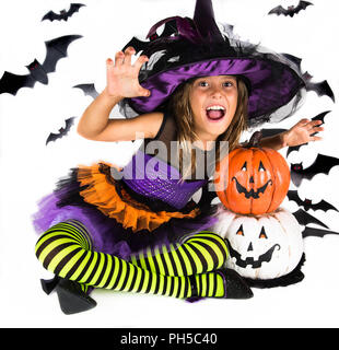 Happy Halloween witch & happy pumpkin. Little girl with a Halloween costume of a witch with hat, striped legs holding two smiley Halloween pumpkins Stock Photo