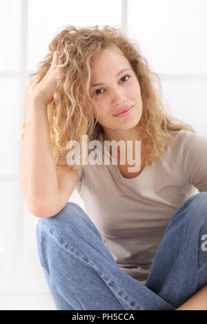 portrait of young woman caressing her long hair, sitting on floor dressed in jeans and T shirt, isolared on white Stock Photo