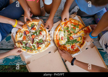 Top view image of children grab slices of pizza from box at the outdoors picnic. Children hands taking pizza Stock Photo