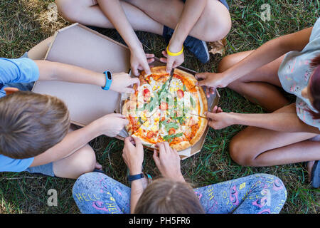 Top view image of children grab slices of pizza from box at the outdoors picnic. Children hands taking pizza Stock Photo