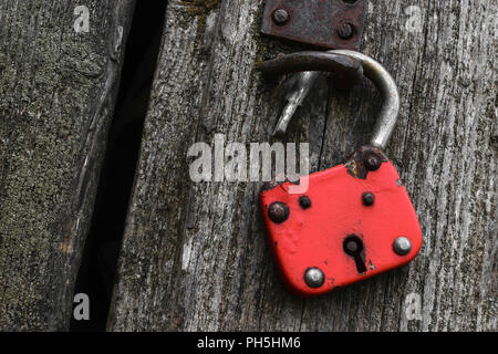 Very old and red lock hanging on grey wooden wall Stock Photo