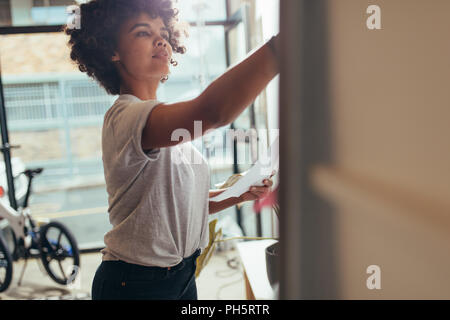 Businesswoman writing on whiteboard at meeting. Young african female working at tech startup writing new project plan on board. Stock Photo