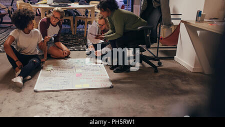 Group of young people discussing over new app development. Four startup colleagues sitting on floor and planning over software and programming for new Stock Photo