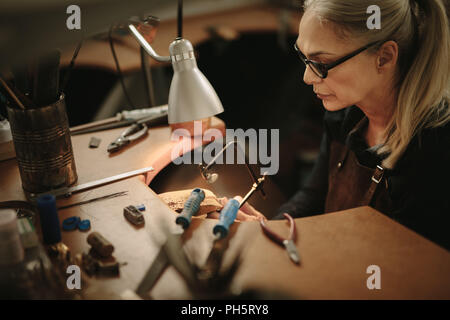 Senior jewelry maker cutting metal with a band saw on workbench. Professional jeweler crafting a ring in her workshop. Stock Photo