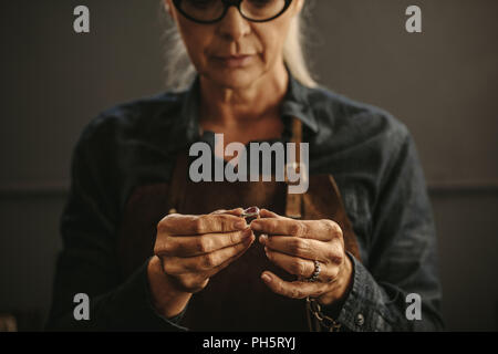 Close up of female jeweler hands examining the silver ring at workshop. Woman goldsmith inspecting jewelry. Stock Photo