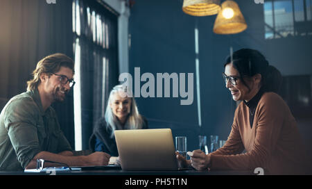 Smiling asian woman giving presenting over laptop to colleagues in meeting room. Happy business professionals meeting in office. Stock Photo