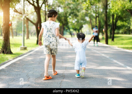 Asian sister hold hands with small children walking on the road in park with rays of sunlight. Stock Photo
