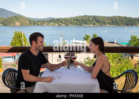 A happy in love couple on an outdoor restaurant patio with a view to the harbor toasting with wine. Stock Photo