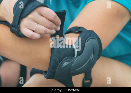 Woman rollerskater putting on elbow protector pads on her hand and wearing wrist guards Stock Photo