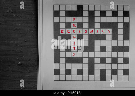 Economics and profits written in red as solutions to a newspaper crossword puzzle on wood Stock Photo