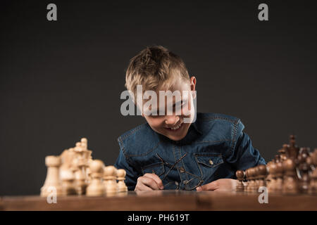 happy little boy holding eyeglasses and looking at chess board at table isolated on grey background Stock Photo