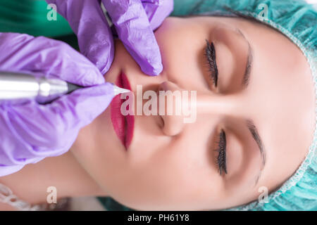 Professional apply procedure of permanent makeup on woman lips in beautician salon. Top view, close up, selective focus Stock Photo