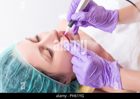 Professional permanent makeup applying on woman lips in beauty studio. Cosmetologist tattooing micro pigmentation lips with professional tools Stock Photo