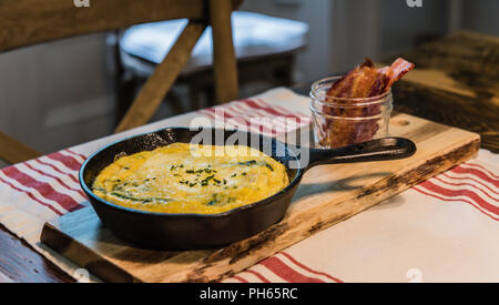 Savory omelette presented in iron skillet and bacon served upright in mason jar. Stock Photo