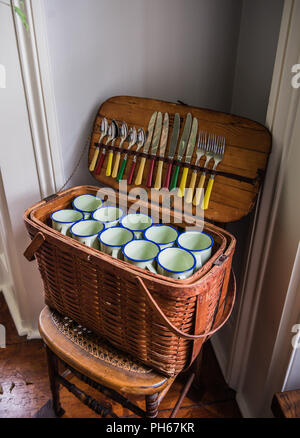 Open retro wicker picnic basket filled with white cups and silverware. Stock Photo