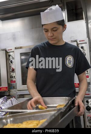 Poland (June 30, 2018) Culinary Specialist 3rd Class Katheryn Salazar, from Winnie, Texas, places mozzarella sticks into a pan in the galley aboard the Harpers Ferry-class dock landing ship USS Oak Hill (LSD 51) in Gydnia, Poland, June 30, 2018. Oak Hill, home-ported in Virginia Beach, Virginia, is conducting naval operations in the U.S. 6th Fleet area of operations. Stock Photo