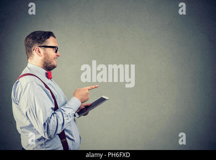 Side view of chunky man in glasses holding tablet and pointing away in choice on gray background Stock Photo
