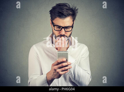 Clueless young man having troubles with his smartphone looking preoccupied Stock Photo