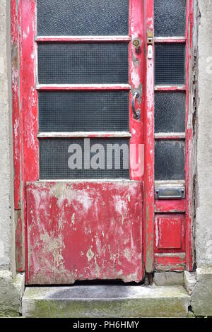 Weathered wooden door with red paint peeling off. Wooden frame is rotting. Stock Photo