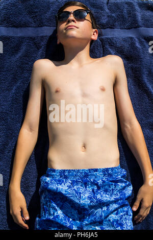 Caucasian teenage boy sunbathing in a garden wearing sunglasses