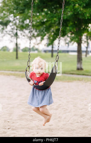 Portrait of happy smiling little toddler girl swinging on swings at playground outside on summer day. Happy childhood lifestyle concept. Toned with fi Stock Photo