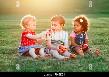 Group portrait of three white Caucasian and latin hispanic children boy and girls sitting together sharing and eating apple food. Love friendship chil Stock Photo