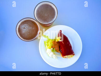 Red stuffed paper with salad and sauce on white plate and two beers, blue background Stock Photo