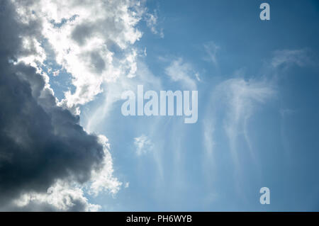 Edge of dark cloud formation backlit by sun with lighter wispy clouds against a blue sky Stock Photo