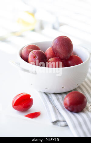 Fresh plums in a colander on a striped cloth Stock Photo