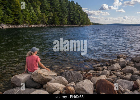 Woman sitting on the shore of the Quabbin Reservoir in New Salem, Massachusetts Stock Photo