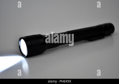 Black LED flashlight turned on with a white background. Simple plain white background lets black illuminated flashlight stand out. Stock Photo