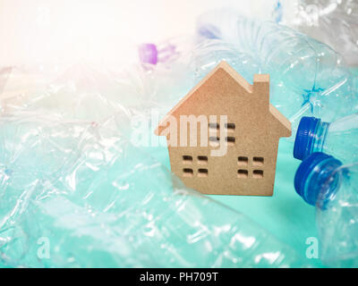 Wooden house and empty crushed recycle clear plastic drink water bottles on blue background with light and copy space. Global warming concept. Stock Photo