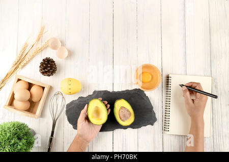 Female hands make notes in diet book , Top view, concept, copy space, hand holding avocado Stock Photo