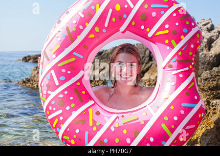 Cheerful young woman holding a pink inflatable doughnut at the adriatic sea, Croatia Stock Photo