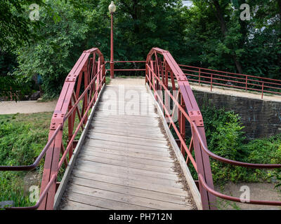 Narrow wooden bridge with red steel guards leading to footpath around canal area Stock Photo
