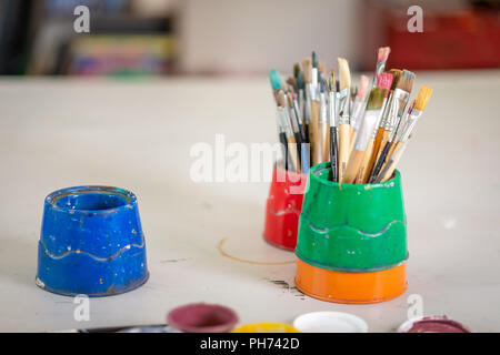 Pots of artist's used paint brushes on a school desk photographed in the art classroom Stock Photo