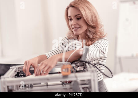 Pretty adult smiling woman adjusting 3D printer Stock Photo