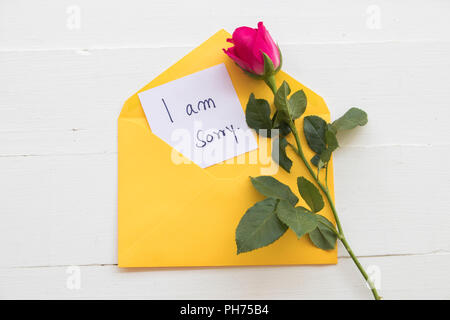 i am sorry message card handwriting in yellow envelope with red rose flower on background white wood Stock Photo