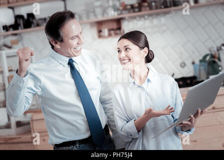 Smiling woman pointing to the laptop and looking at the happy man Stock Photo