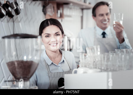 Pretty waitress smiling while standing near the coffee machine Stock Photo