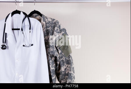 Medical white consultation coat and military uniform on hanger Stock Photo