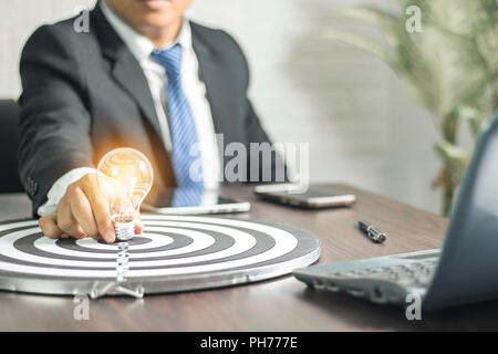 Idea concept,Businessman holding light bulb on dart board to goal on desk Stock Photo