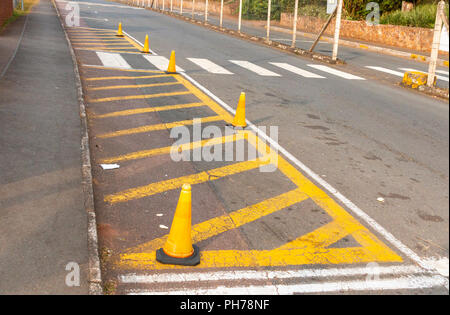 A painted island outside a preschool conered off by orange road cones next to a zebra crossing between two busy roads Stock Photo