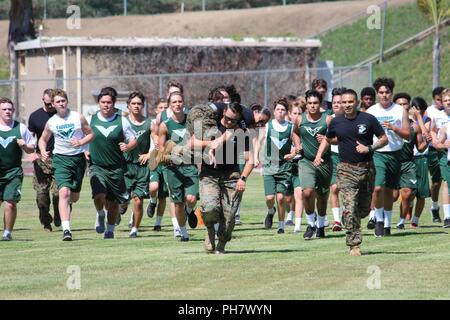 Marine Sgt. Phillip Kelso buddy carries Sgt. Kirsten Vandusen alongside Gunnery Sgt. Christopher Mondragon to demonstrate a portion of the Combat Fitness Test with students of Irvine High School, Irvine, Calif., on June 28, 2018. These football players executed the CFT with local recruiters of Marine Corps Recruiting Station Orange County to enhance their overall fitness and learn more about athleticism within the Marine Corps. Stock Photo