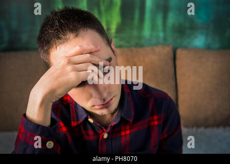 Portrait of sad upset young guy. The brooding man sitting and holding a hand over his head. In a bad mood. depression. headache, head pain Stock Photo